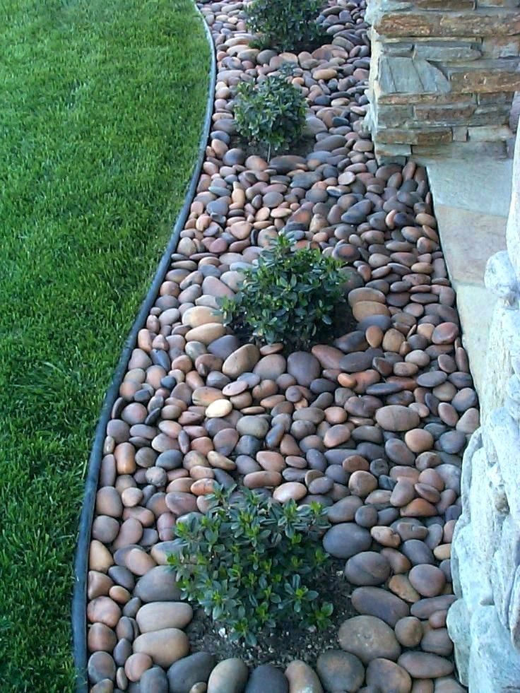 a garden with rocks and plants in the grass next to a stone path that is lined with green grass