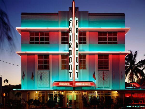 an art deco building lit up with red, white and blue lights at night in front of palm trees