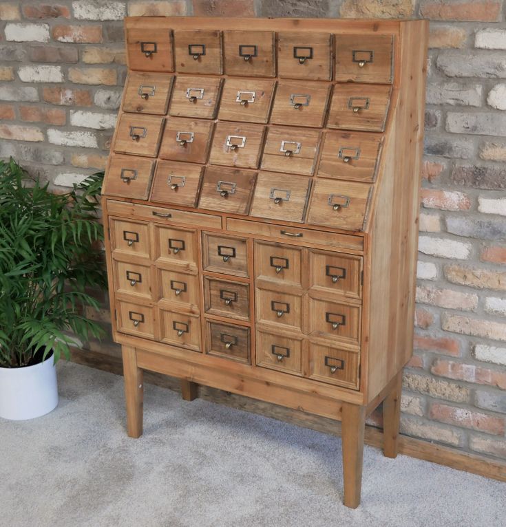 a wooden cabinet with many drawers in front of a brick wall next to a potted plant