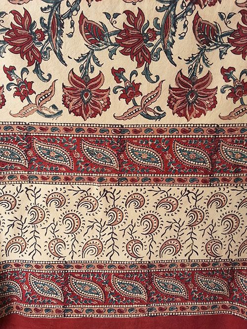 an old red and white cloth with floral designs on the border, sitting on a table