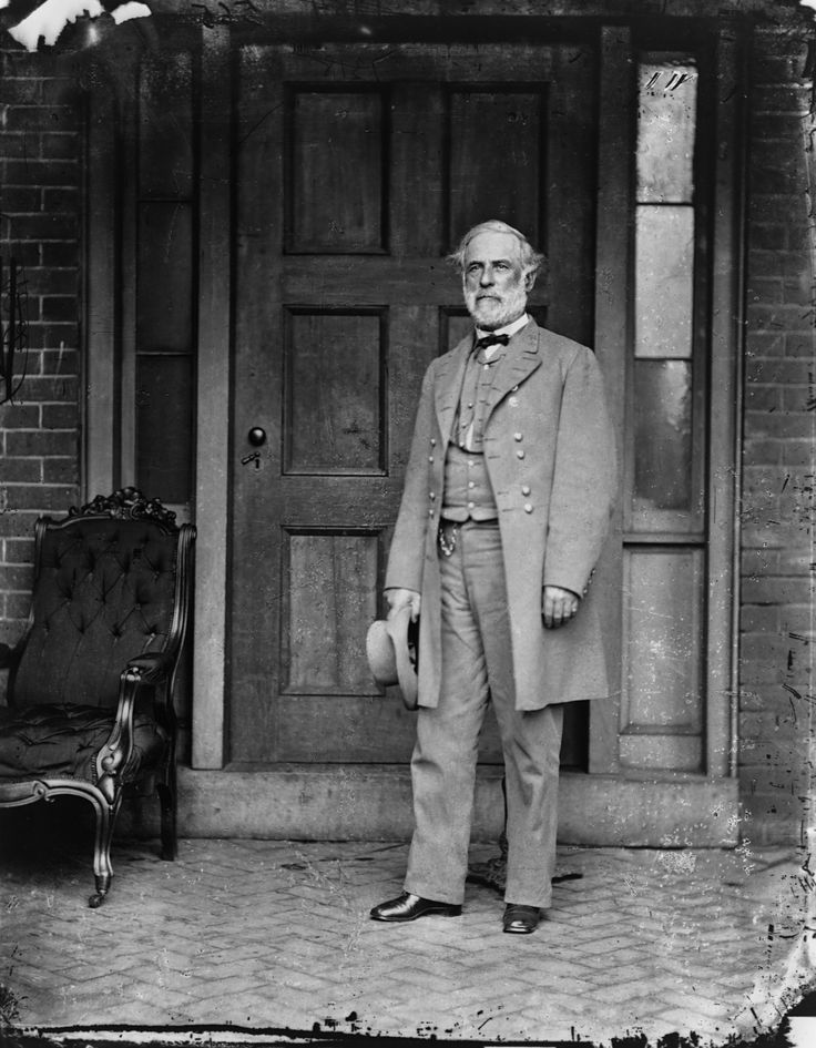 an old black and white photo of a man standing in front of a door wearing a suit