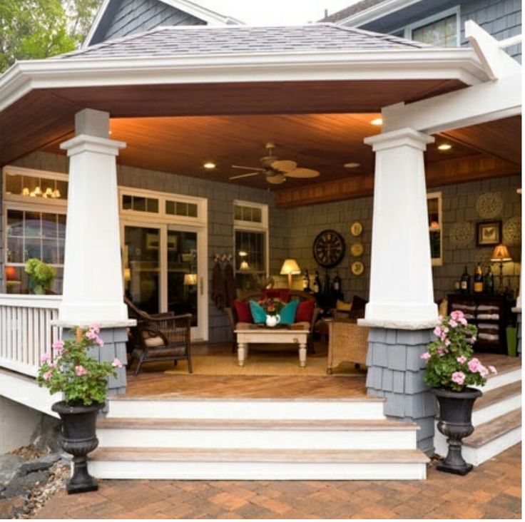 a covered porch with two planters on the steps and an outside living room in the background