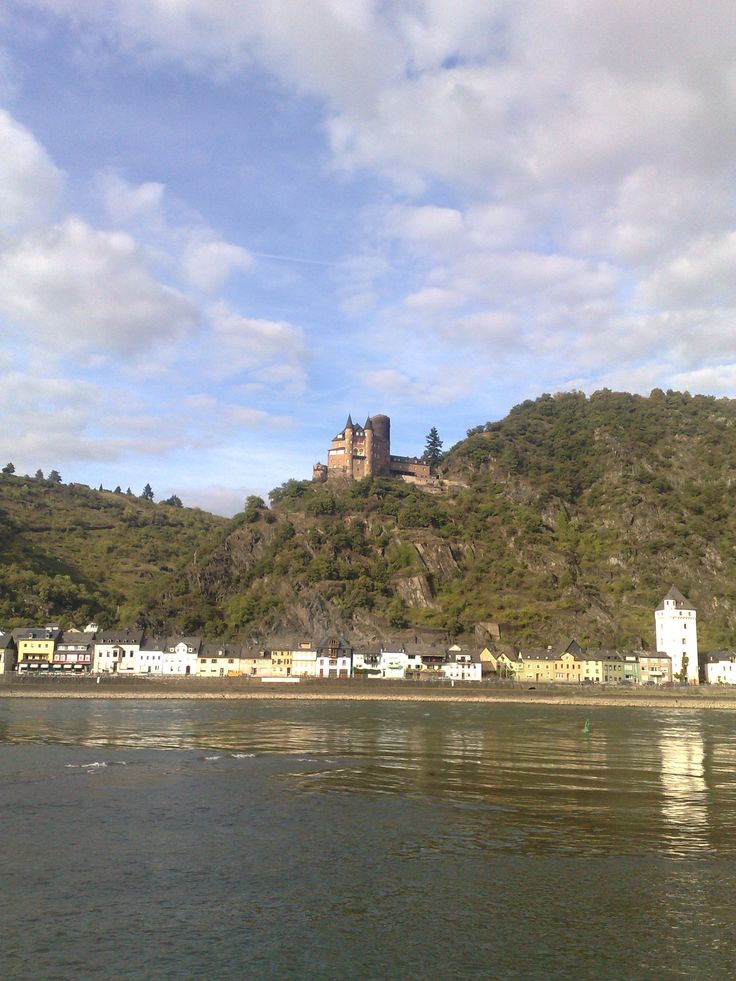 an old castle on top of a hill next to the water with buildings below it