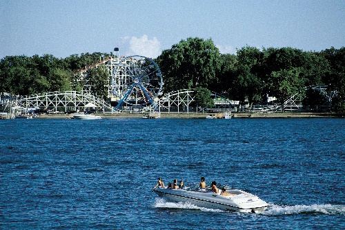 a group of people riding on the back of a white boat in front of a ferris wheel