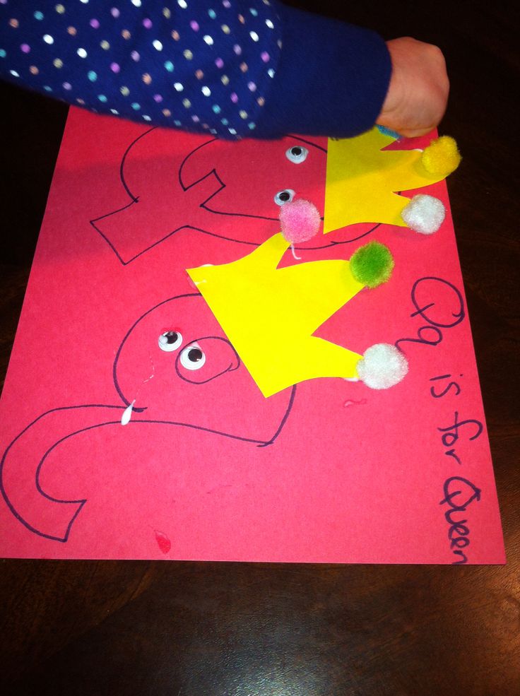 a child's hand holding a paper crown on top of a piece of pink paper