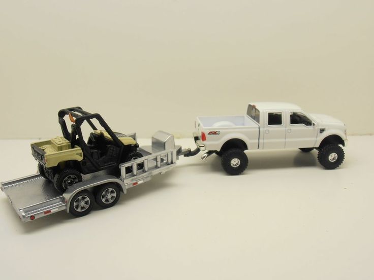 two toy trucks pulling a trailer on a white surface