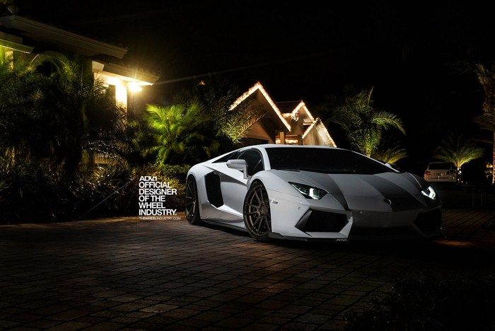 a white and black sports car parked in front of a house at night with lights on