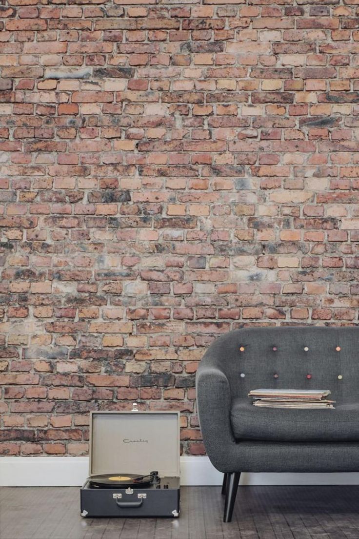 a grey couch sitting in front of a brick wall next to a suitcase and record player