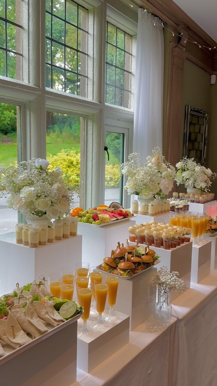 an assortment of food and drinks on display in front of large windows at a wedding