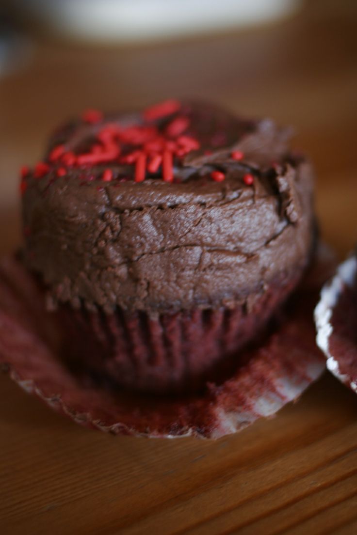 two chocolate cupcakes with red sprinkles sitting on a wooden table