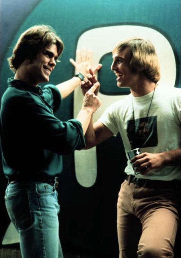 two young men standing next to each other in front of a green and white sign