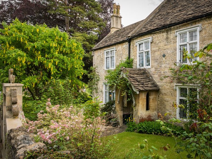 an old stone house surrounded by trees and flowers