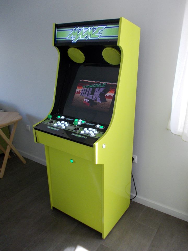 a green arcade machine sitting on top of a hard wood floor next to a window