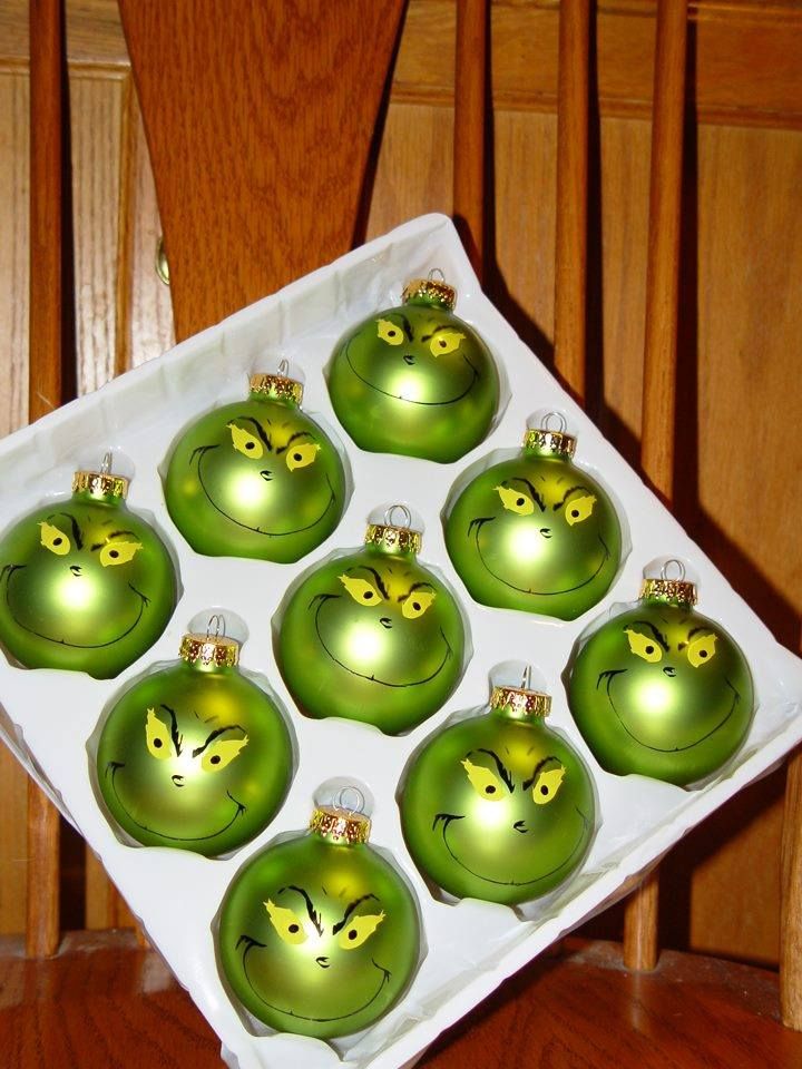 twelve green glass christmas ornaments with yellow eyes on them sitting in a white square box