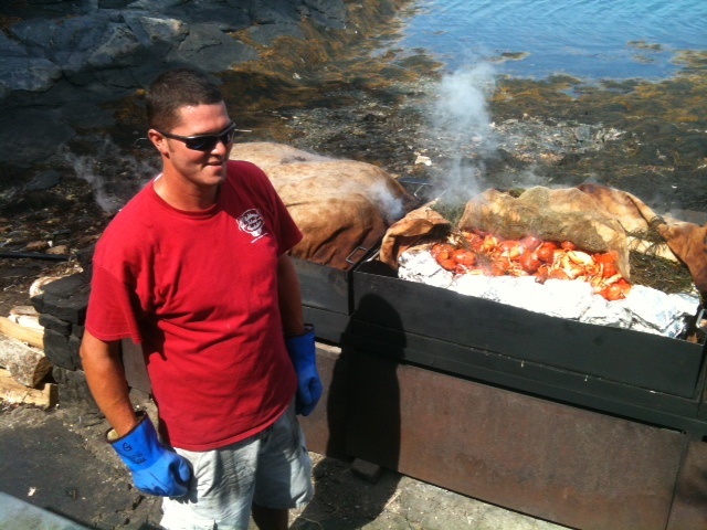 a man standing in front of a grill with food on it and water behind him