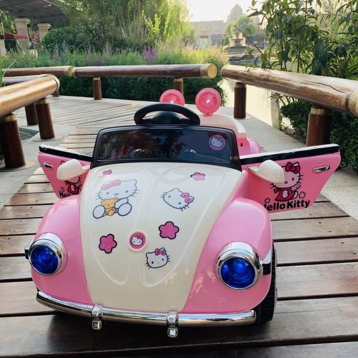 a pink and white car with hello kitty decals on the front is sitting on a wooden platform