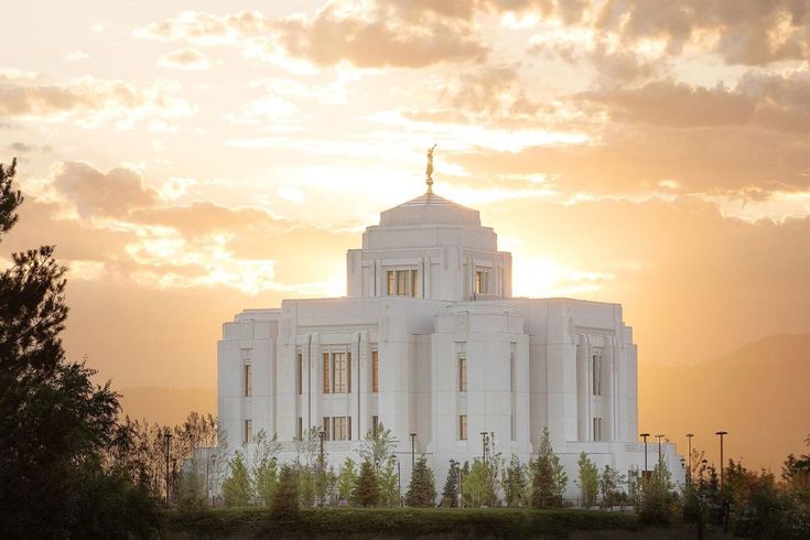 a large white building with a cross on top and trees in the foreground at sunset