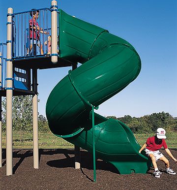 a man sitting on top of a slide next to a green playground structure with a blue sky in the background