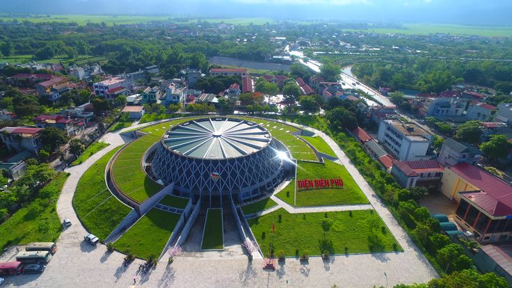 an aerial view of a circular building in the middle of a green area with trees and buildings around it