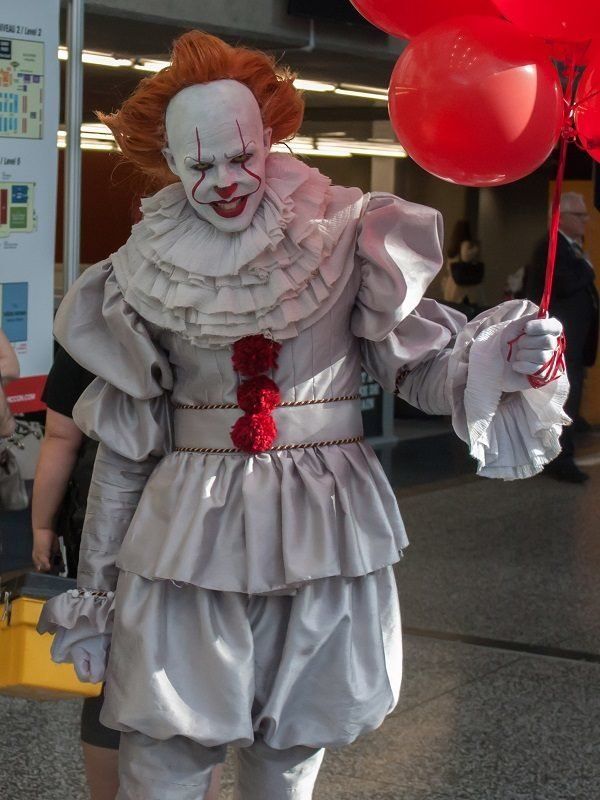 a creepy clown with red hair and white makeup is walking down the street holding balloons