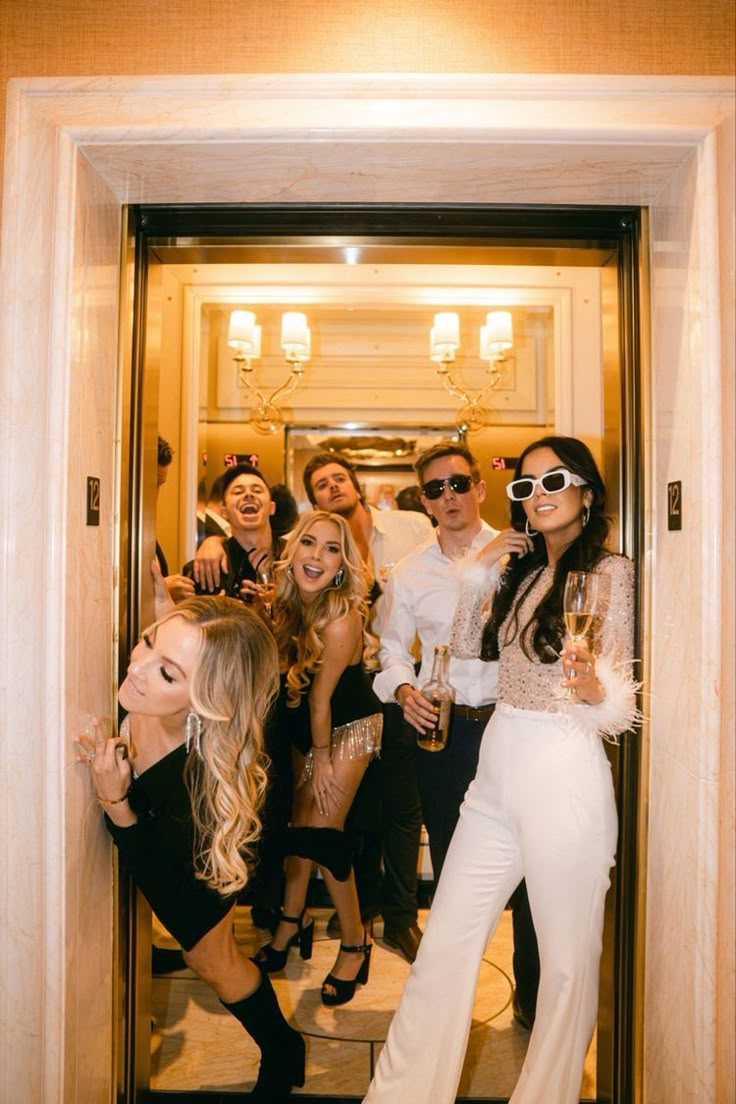 a group of people standing around each other in front of a door holding champagne flutes