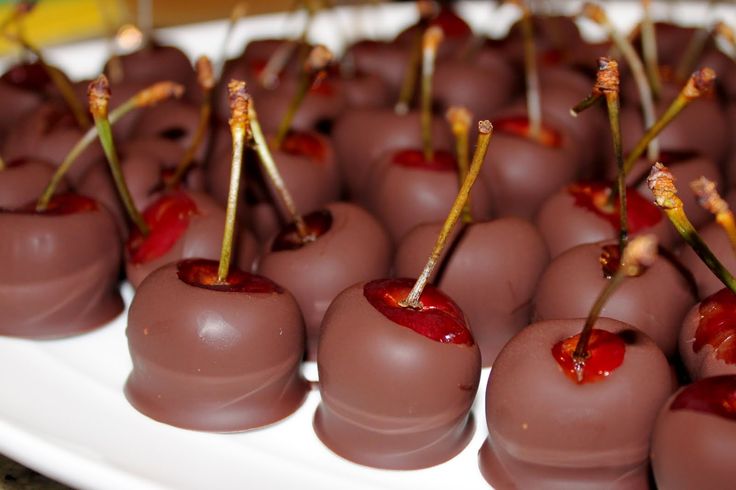 chocolate covered cherries on a white platter with toothpicks sticking out of them