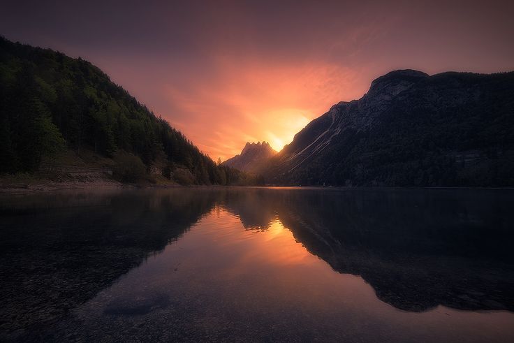 the sun is setting over a mountain lake