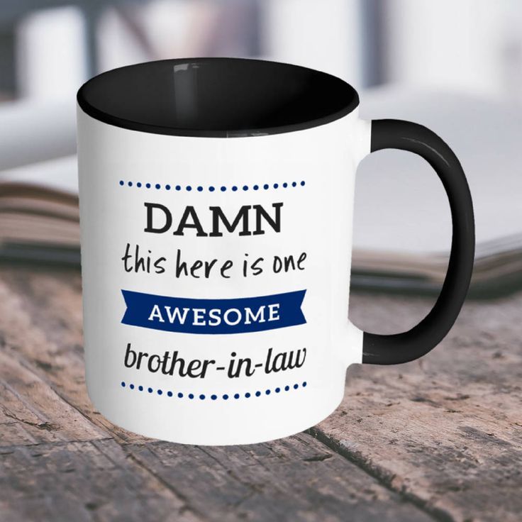 a black and white coffee mug sitting on top of a wooden table next to an open book