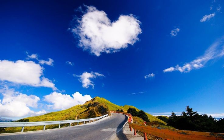 a heart shaped cloud is in the blue sky above a road with orange railings