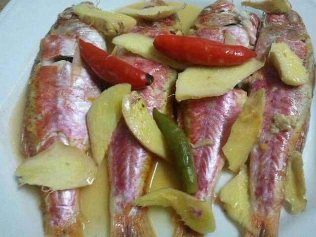 some fish and potatoes on a white plate with red peppers in the middle, along with other food items