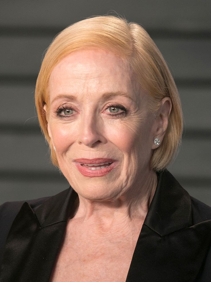 an older woman with blonde hair wearing a black suit and diamond earrings on her left ear