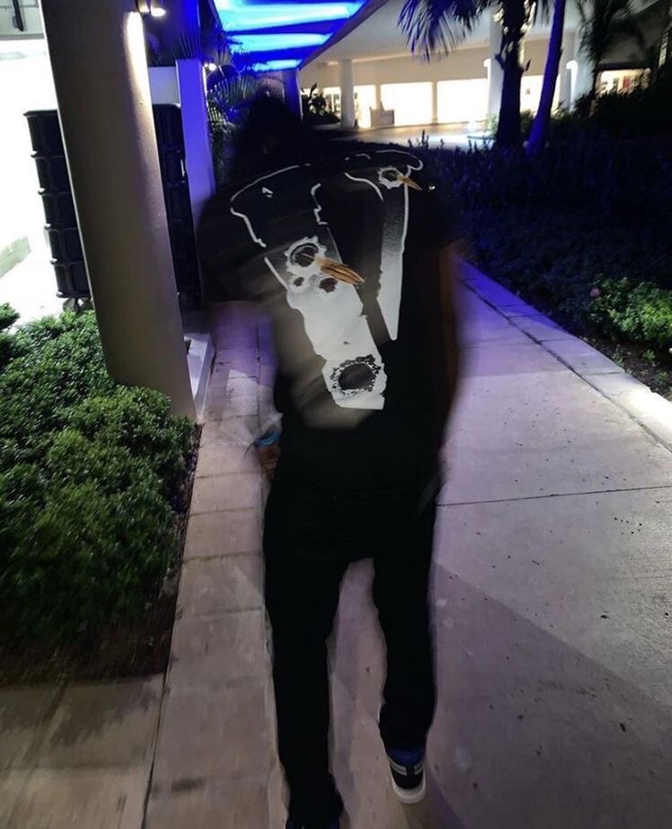 a man is walking down the sidewalk at night with his back turned to the camera