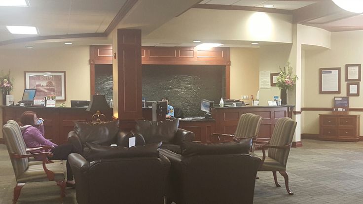 an empty waiting room with two people sitting in chairs and one person standing at the front desk