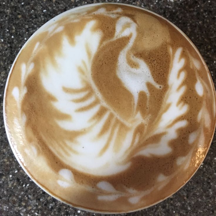 a white and brown bowl with designs on it sitting on a counter top next to a cup of coffee