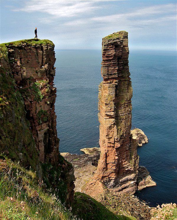 a person standing on top of a cliff next to the ocean with two tall rocks sticking out of it