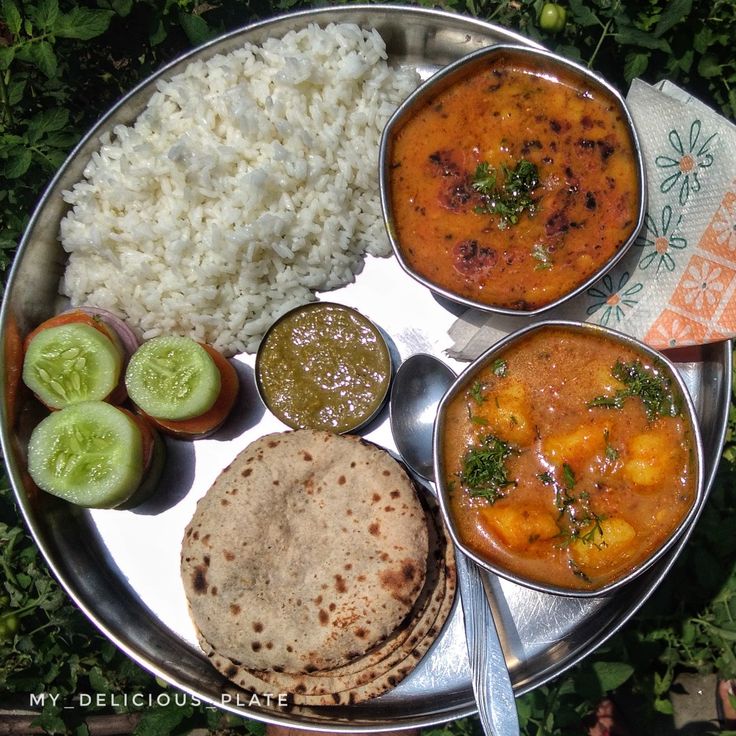 a metal plate topped with rice and different types of food next to cucumbers