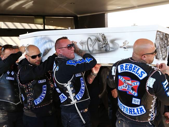 several men in leather jackets and sunglasses are standing near a large white object with blue lettering on it