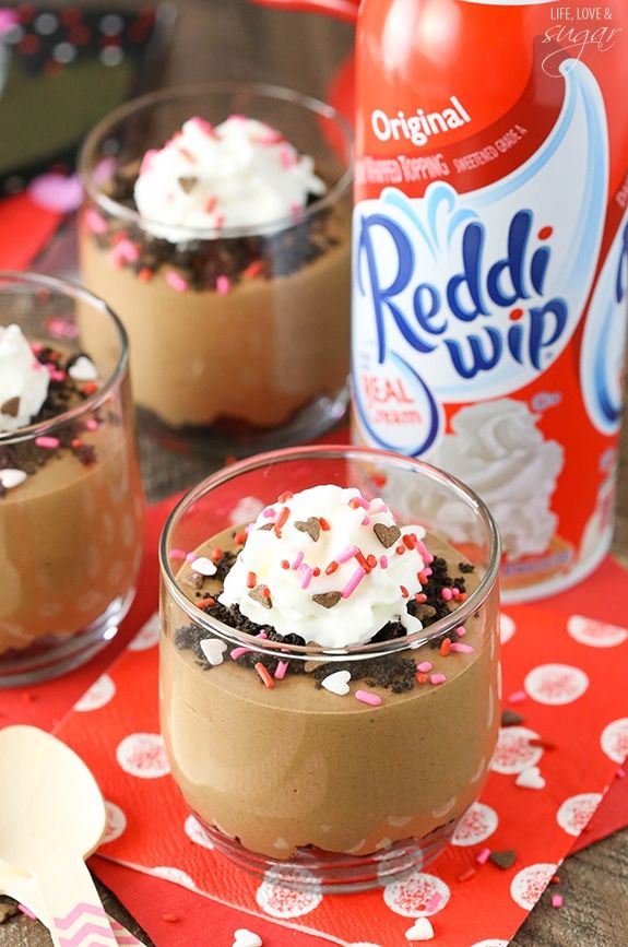 two desserts with sprinkles and whipped cream in small glasses on a table