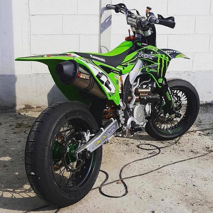 a green and black dirt bike parked next to a white building with a motorcycle on it's side