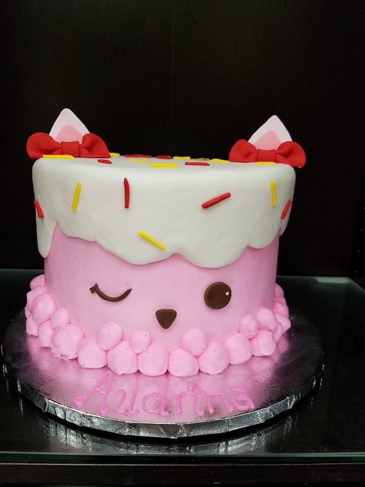 a pink cake with white frosting and red bows on top is sitting on a black surface