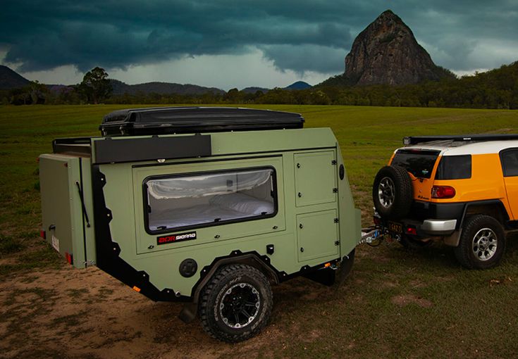 an off - road camper trailer parked next to a jeep in the middle of a field