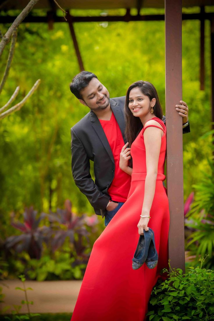 a man and woman standing next to each other in front of some trees with green plants