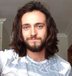 a man with long hair and beard standing in front of a mirror looking at the camera