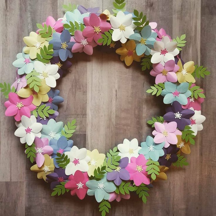 a wreath made out of paper flowers sitting on top of a wooden floor next to a wall