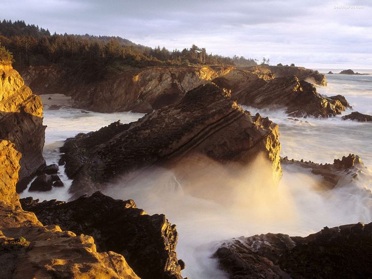 waves crash on the rocky shore at sunset