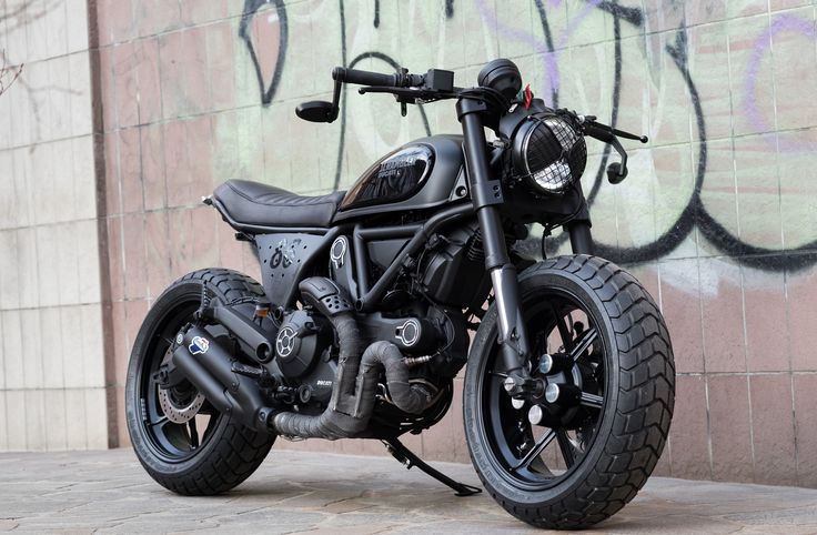 a black motorcycle parked in front of a wall with graffiti on it's side