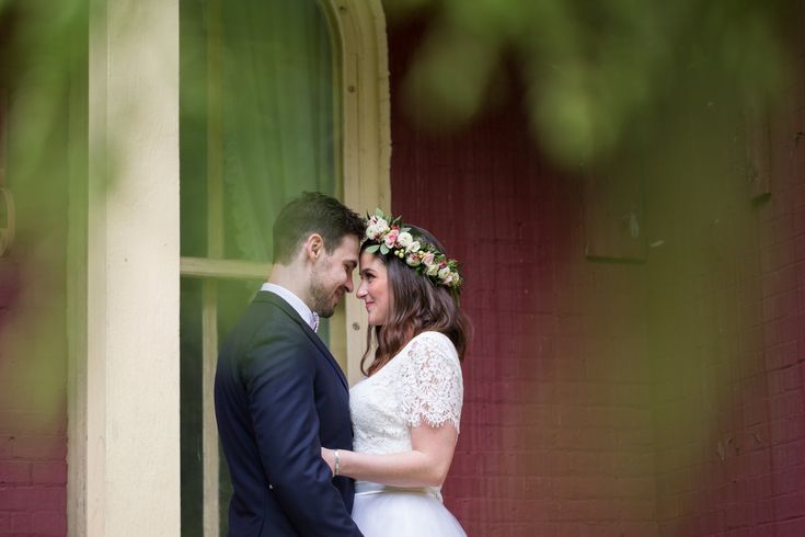 a bride and groom standing in front of a red brick building with their arms around each other