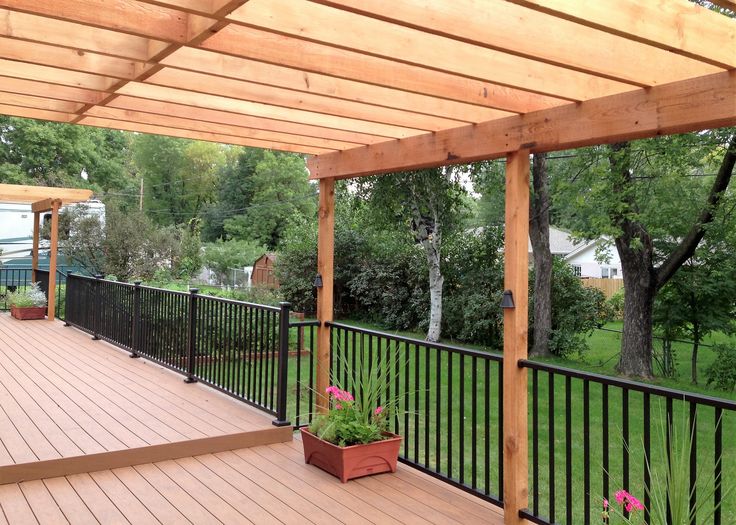 a wooden deck with black iron railings and potted plants on the bottom level