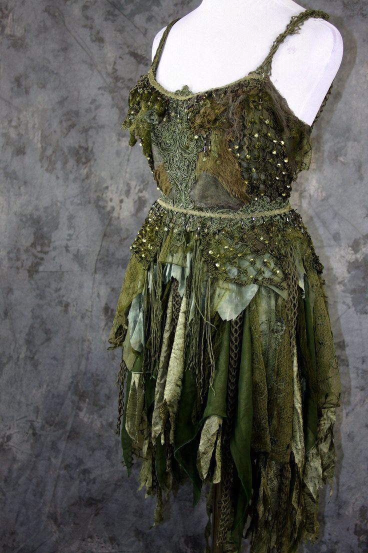 a green dress with sequins and feathers on the skirt is displayed in front of a gray wall