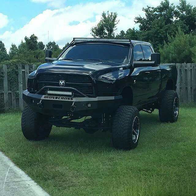 a large black truck parked on top of a lush green field next to a wooden fence